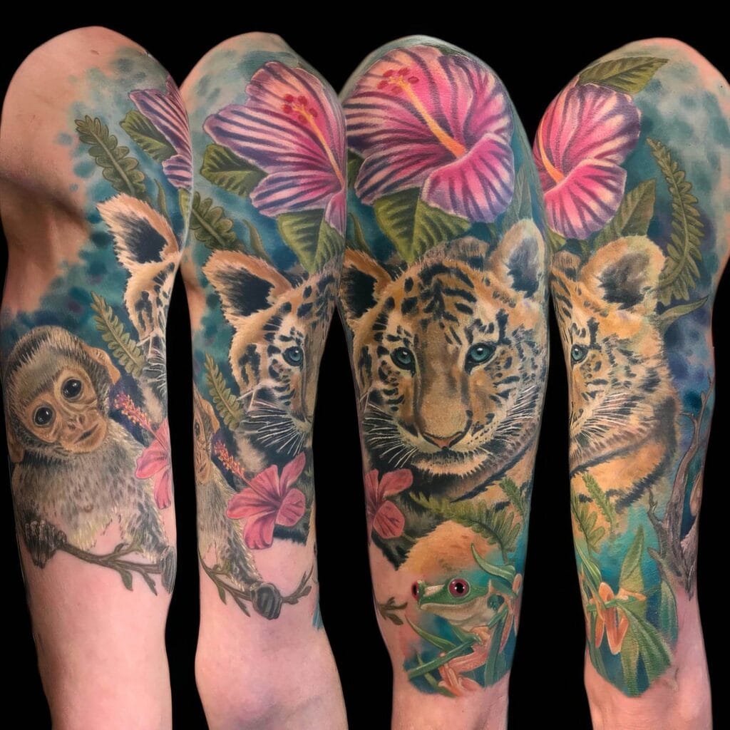 A full sleeve tattoo featuring a baby monkey, tiger cub, and frog among hibiscus flowers and greenery on a person's arm.