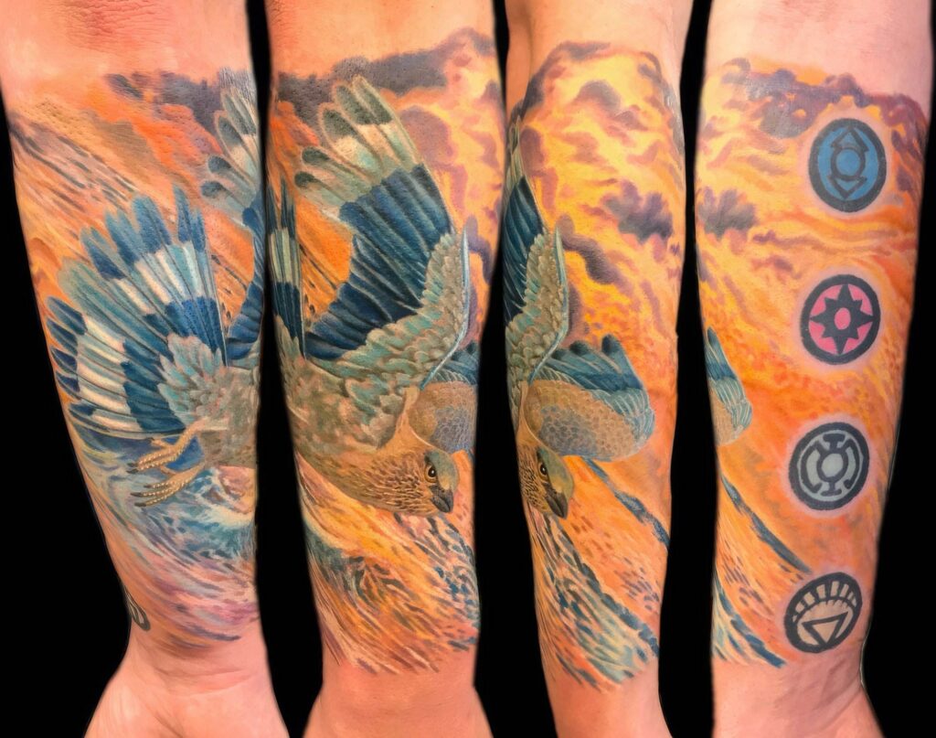 A multi-angle view of a forearm tattoo featuring a detailed blue and grey bird in flight, set against a vivid orange and purple sky with four circular symbols on the side.