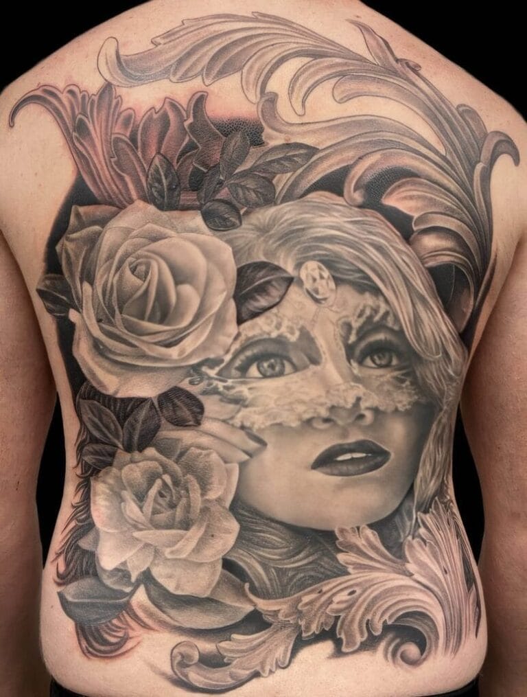 Realistic black and gray tattoo of a womans face surrounded by roses and ornate scrollwork.