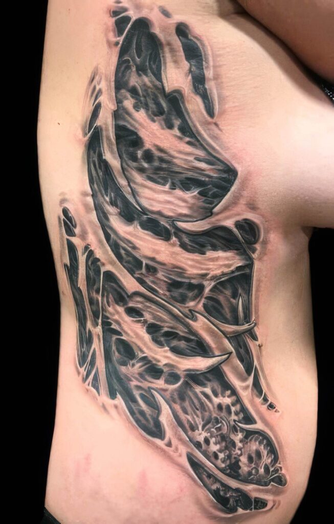 A detailed, black and gray, abstract anatomical tattoo is displayed on a person's side torso, showcasing a blend of organic shapes and patterns against bare skin.