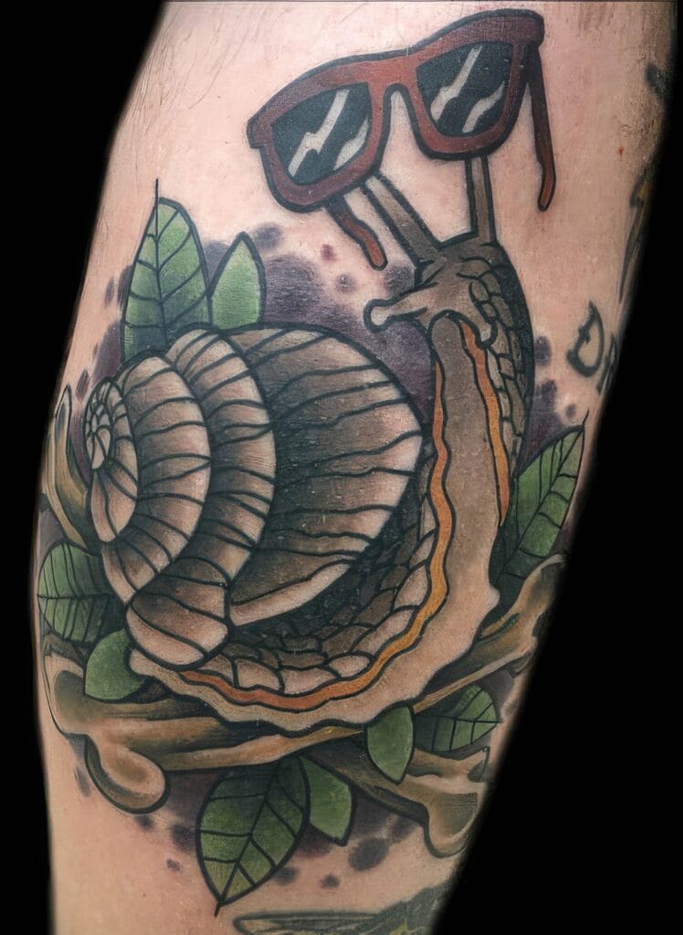 Tattoo of a snail wearing red sunglasses, situated among green leaves and branches on the skin.