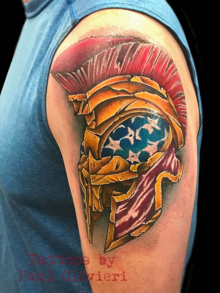 A colorful tattoo of a gladiator helmet with a blue and white star pattern is on an upper arm. The text reads, "Tattoos by Paul Olivieri.