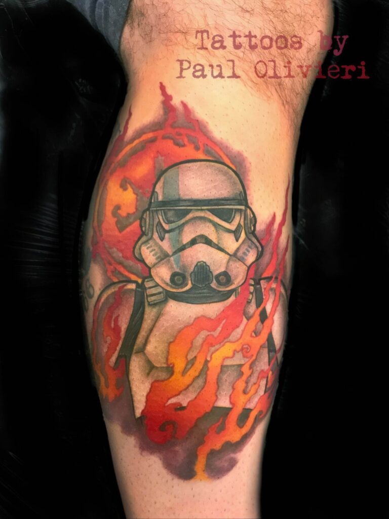 Tattoo of a stormtrooper helmet surrounded by flames on a person's leg, with the text "Tattoos by Paul Olivieri" shown on the top right.