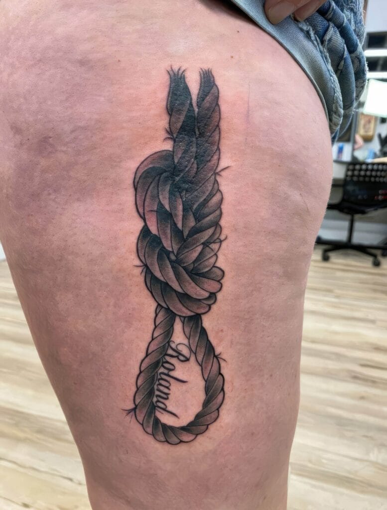 A tattoo of a detailed, shaded rope forming a loop and knot is inked on the back of a person's leg. The word "believe" is incorporated into the bottom part of the rope.