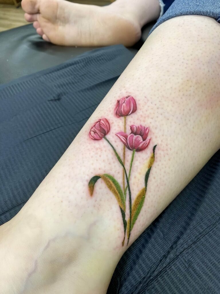 A detailed tattoo of three pink tulip flowers with green leaves on a person's lower leg.