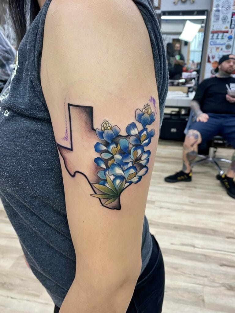 A tattoo on an upper arm features an outline of Texas with bluebonnet flowers inside.