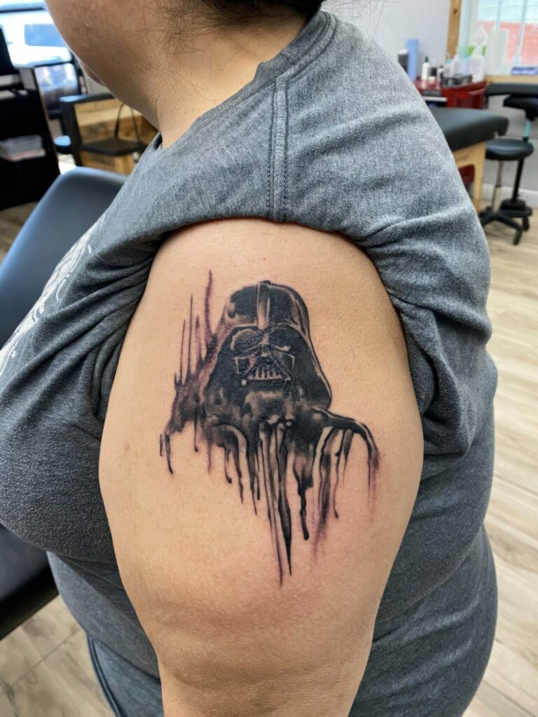 Person with a tattoo of Darth Vader on their upper arm, featuring a dripped ink style.