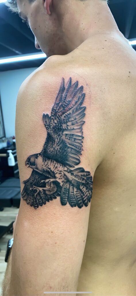 A person with a tattoo of a detailed and realistic bird in flight on their upper arm.