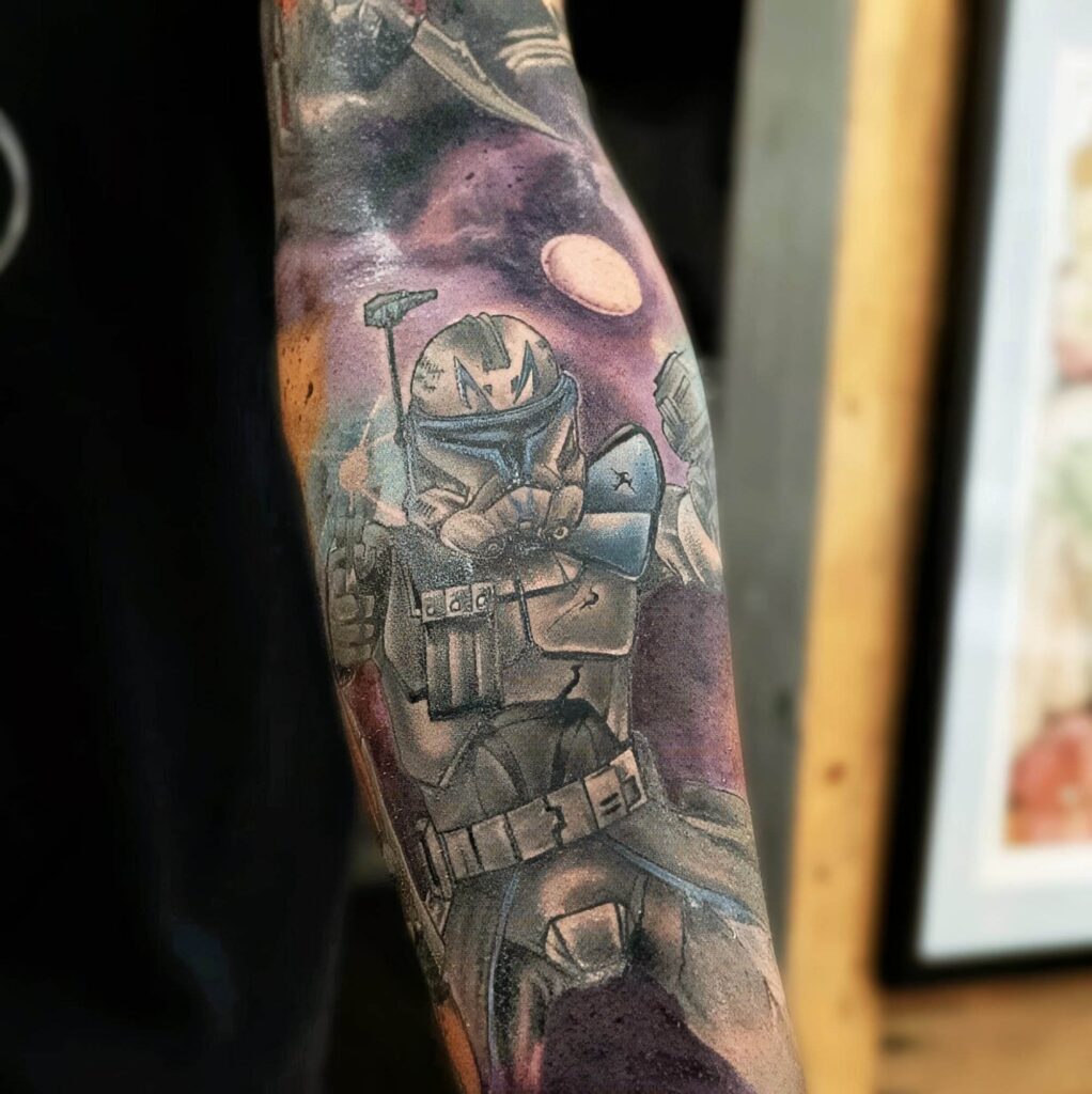 Tattoo of a futuristic soldier in armor with a helmet, holding a weapon, set against a space-themed background on a person's arm.