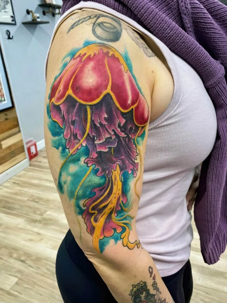 Colorful jellyfish tattoo on persons upper arm with pink, purple, yellow, and blue hues.