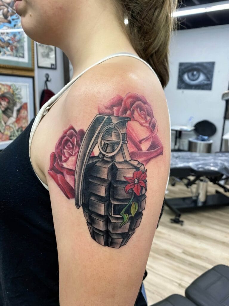 Tattoo of a grenade surrounded by roses, located on a woman's upper arm, in a tattoo studio.