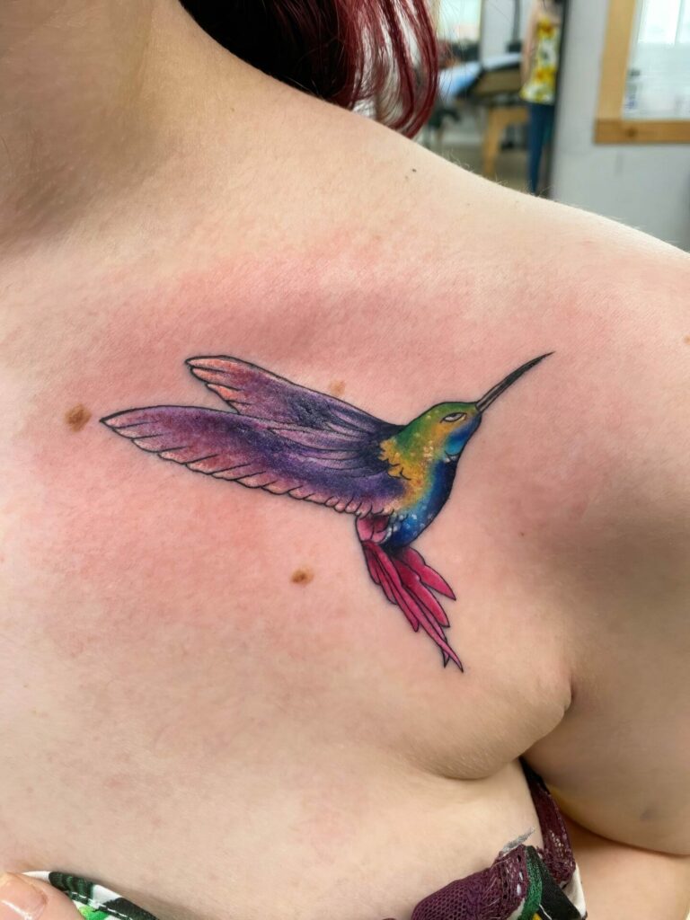 A colorful tattoo of a hummingbird in flight is inked on a person's upper chest.