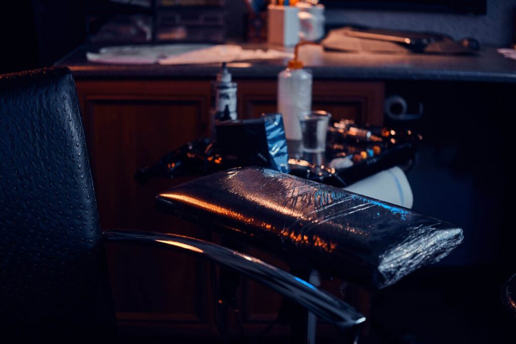 A dimly lit tattoo studio featuring a tattoo chair and a workstation with various inks and tools.