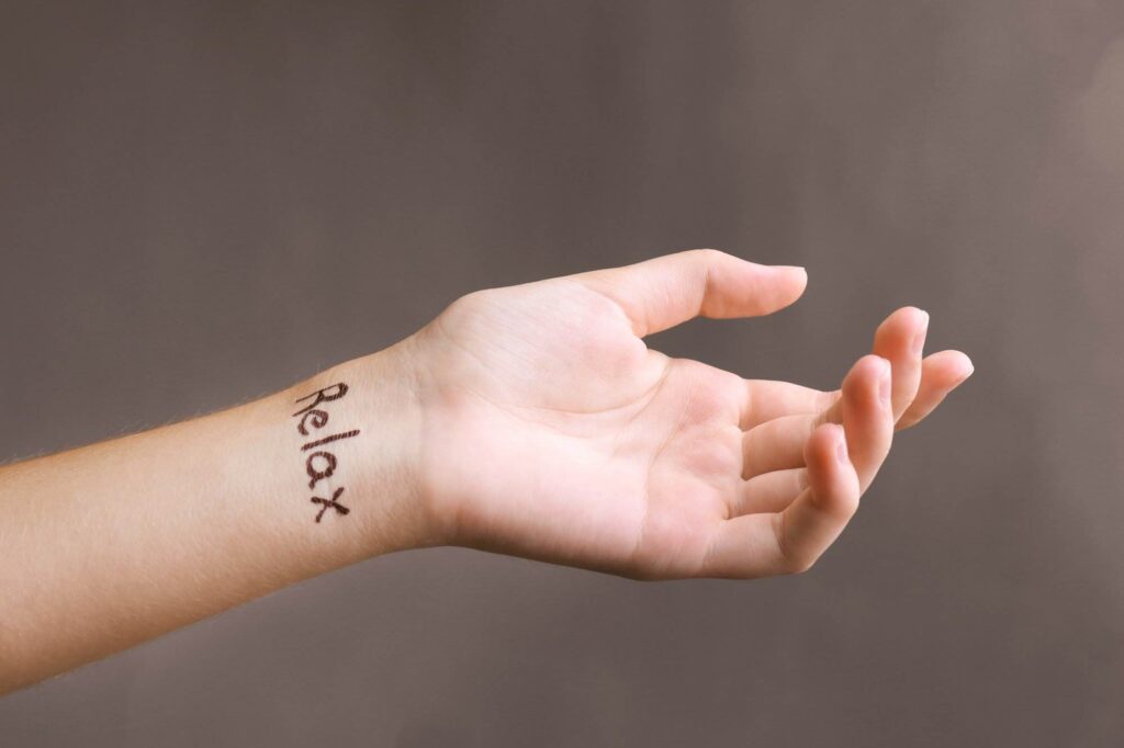 A hand with the word "Relax" written on the wrist in black ink is shown against a plain background.