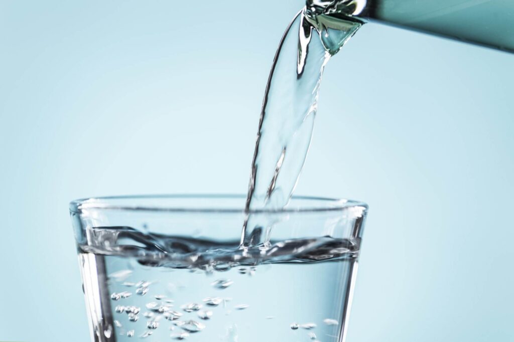 Close-up of water being poured from a pitcher into a clear glass, with bubbles forming as it fills.