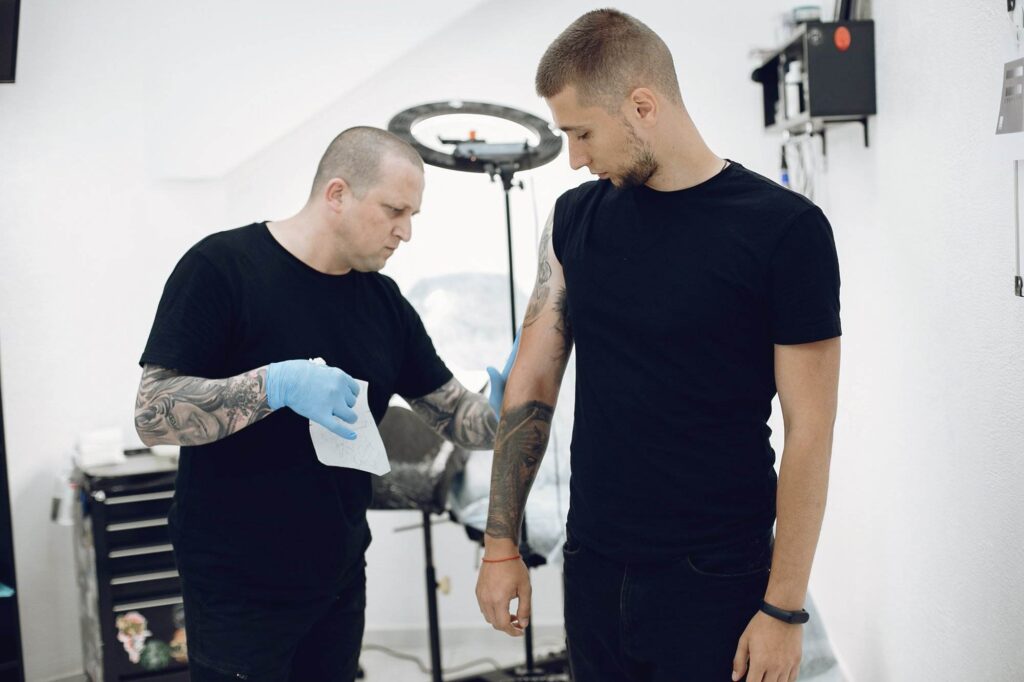 A tattoo artist with gloves prepares a client's arm in a tattoo studio.