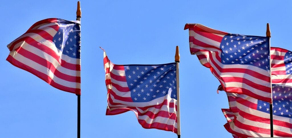 Multiple American flags waving against a clear blue sky.