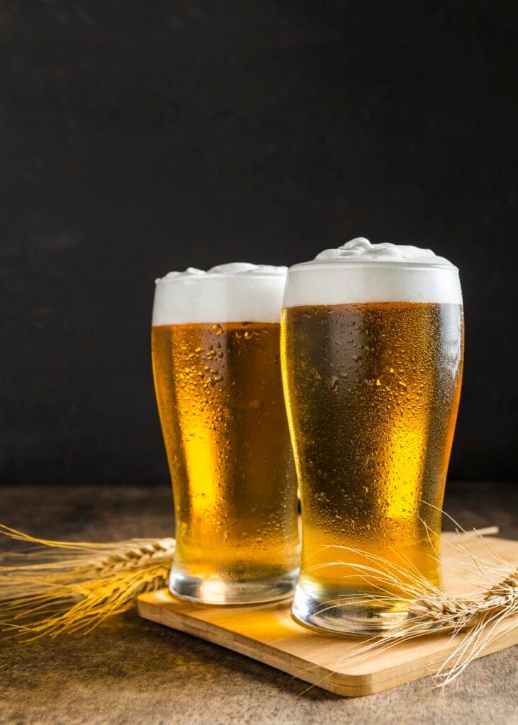 Two glasses of cold beer with foam on top, condensation on the sides, on a wooden tray.