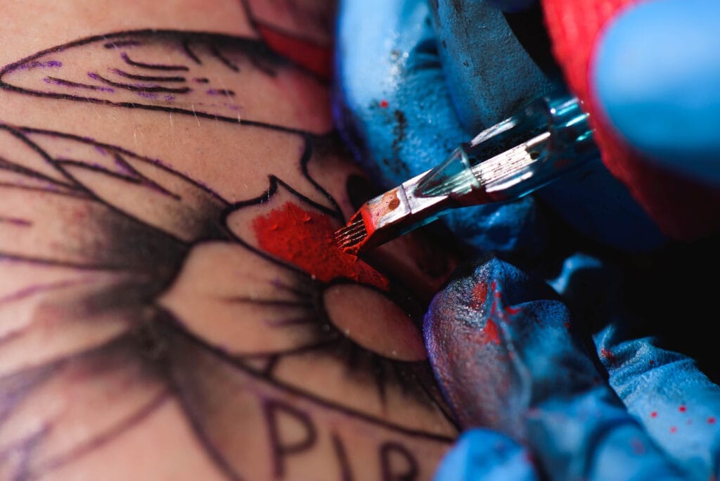Tattoo artist applying red ink to a colorful butterfly tattoo on skin.