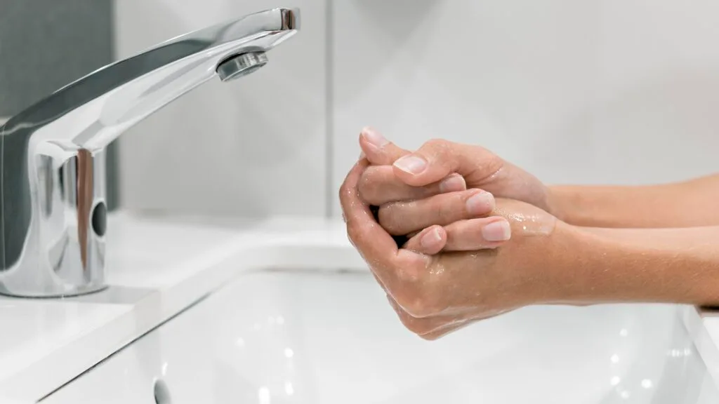 Person washing hands under a faucet with water running.