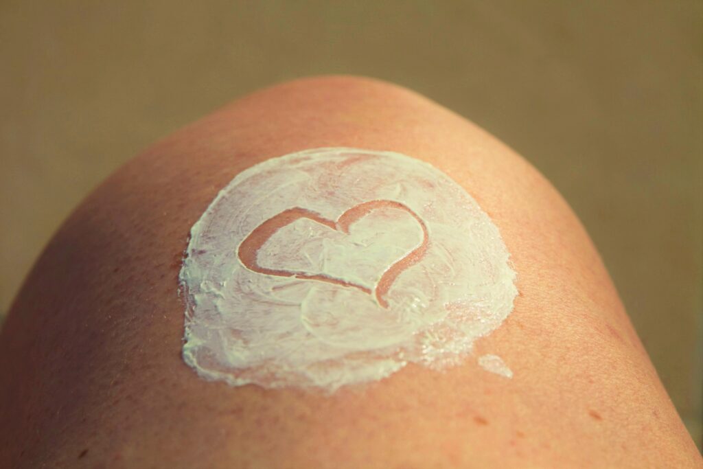 A close-up of a person's skin with a layer of white lotion spread in a circle, featuring a heart shape drawn in the lotion.
