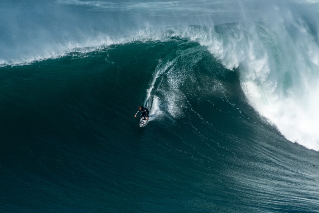 A surfer rides a large, powerful wave in the ocean under natural daylight.