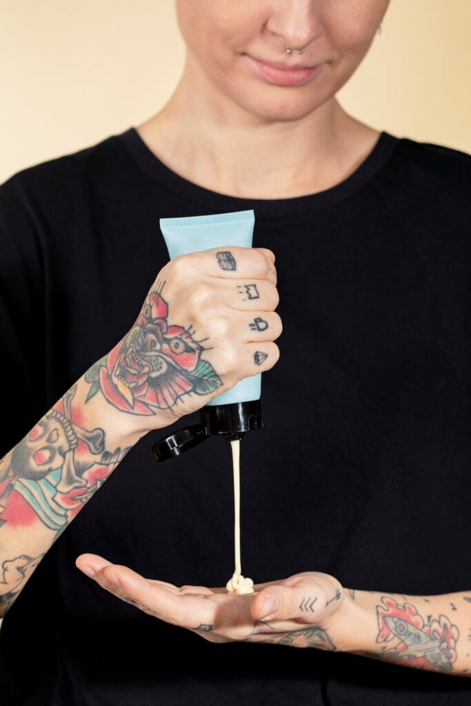Tattooed person squeezing cream from a tube into their open palm.