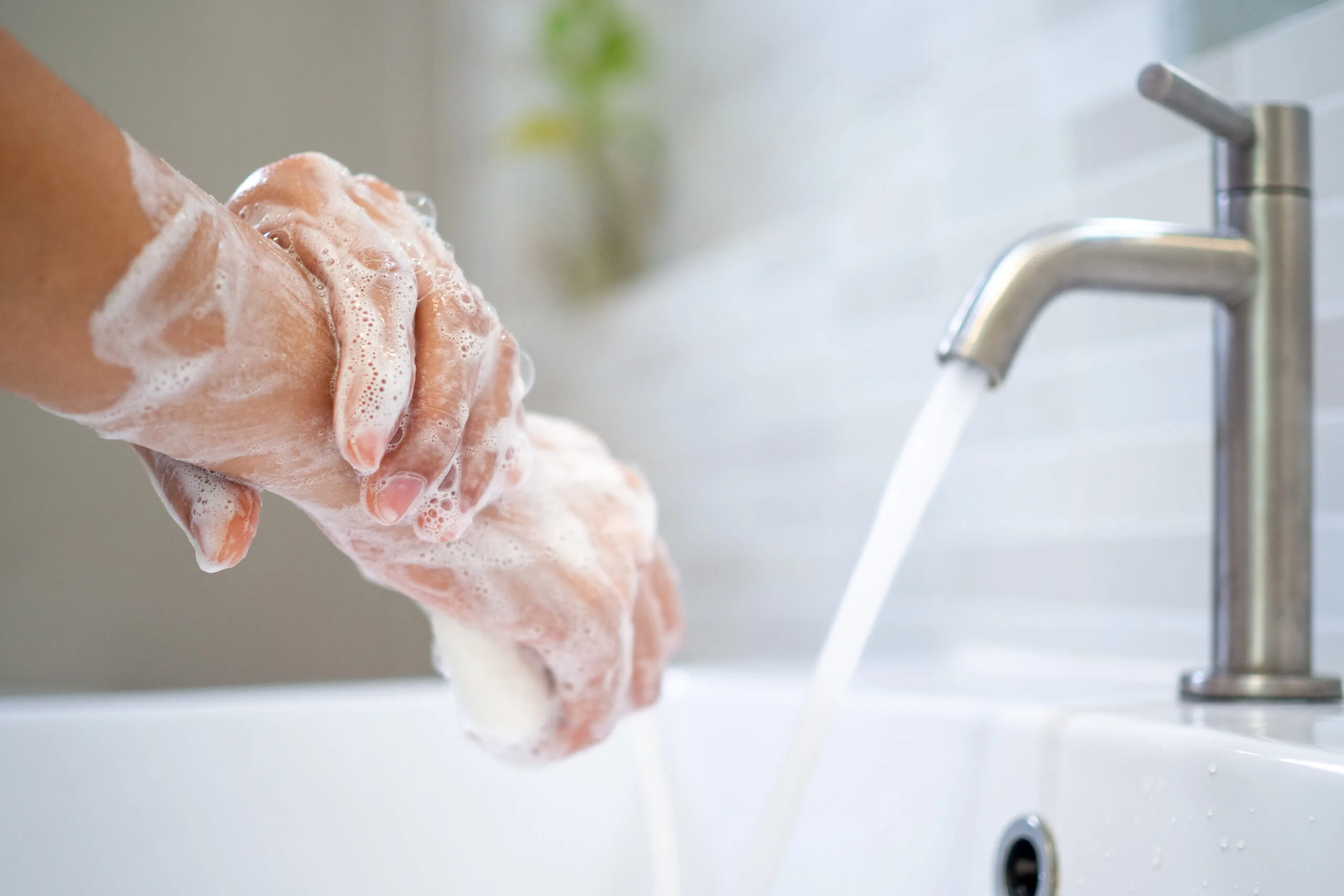 A person washing their hands with soap under running water at a sink.