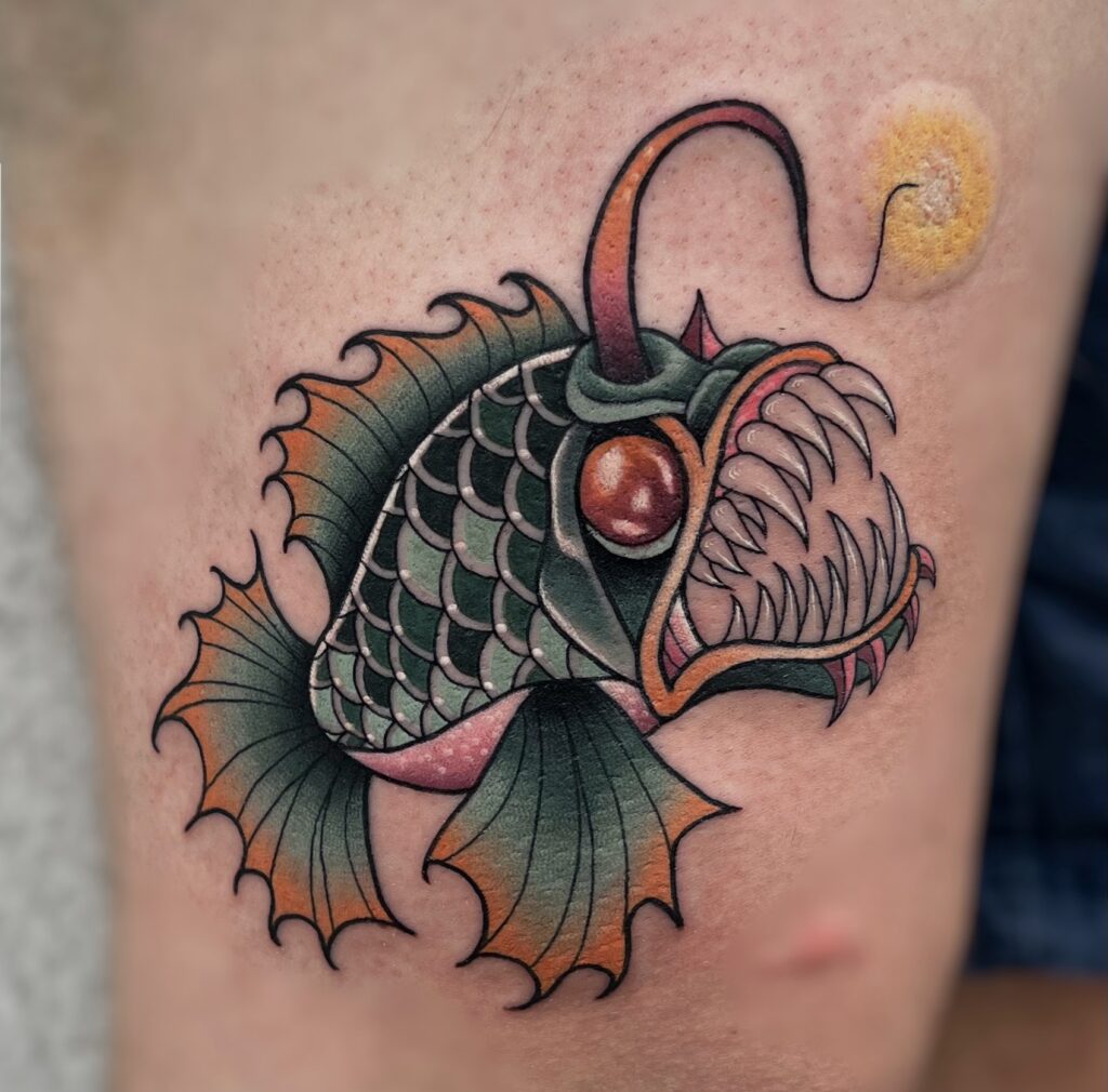Colorful fish tattoo with sharp teeth, large eye, and detailed fins on skin.