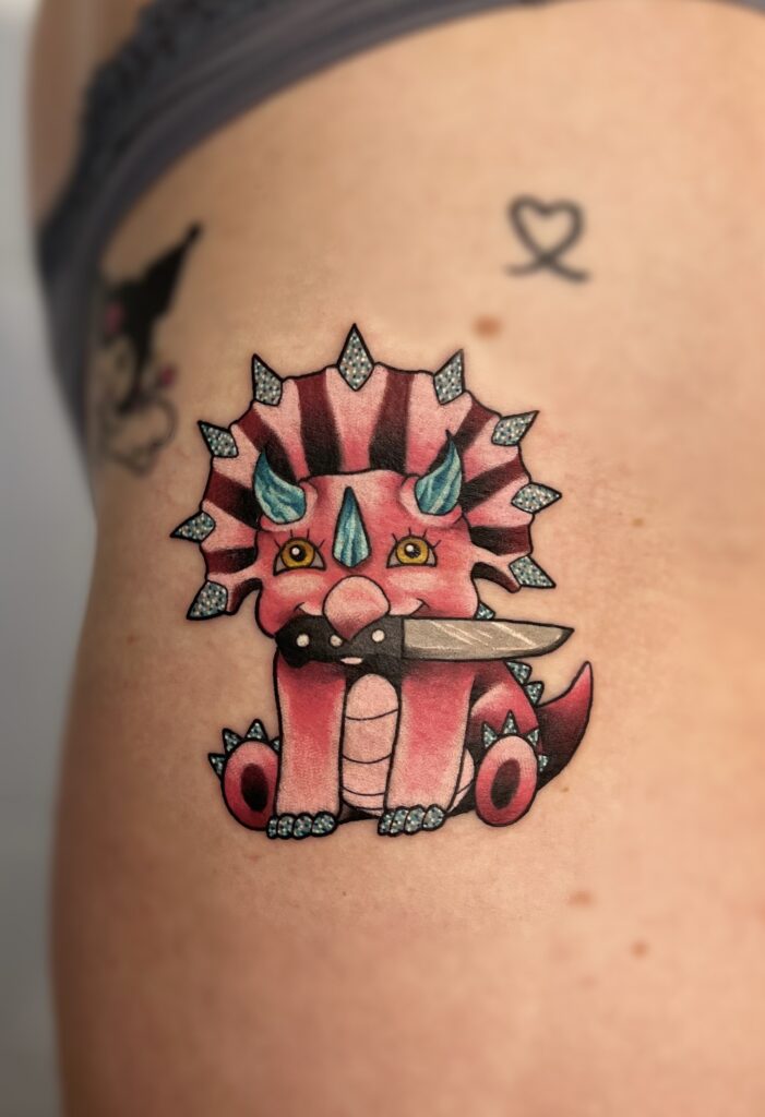 Colorful cartoon-style dragon with a sword in its mouth, sitting with big eyes.