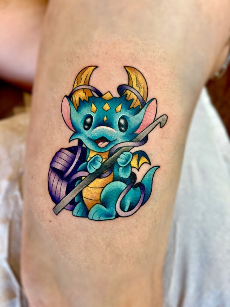 Colorful cartoon dragon tattoo with horns, wings, and a staff.