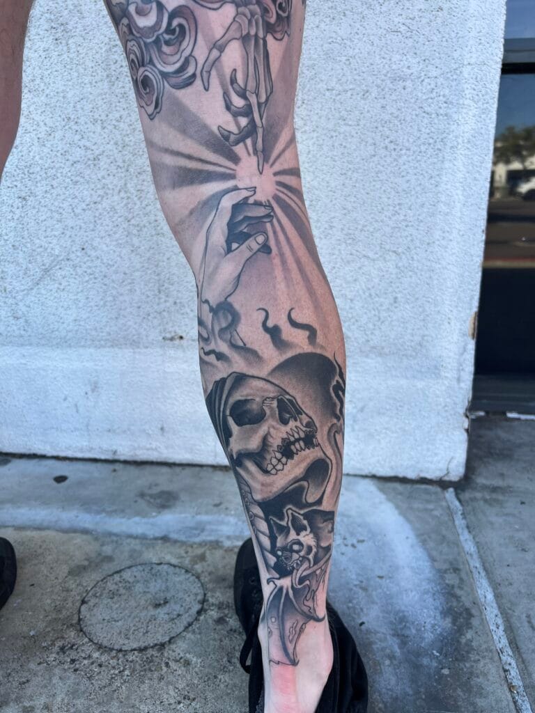 Tattoo of a skull, a cat, and hands with rays emanating from a central point on a persons leg.