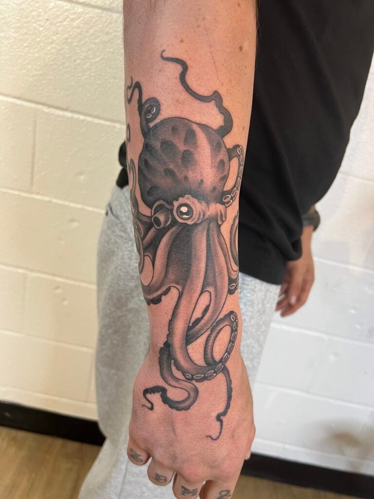 Black and gray octopus tattoo on persons forearm with detailed tentacles and a moon-like head.