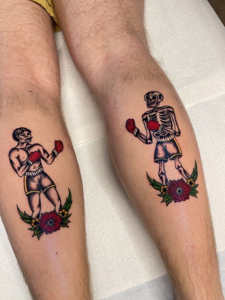 Two tattoos of boxers with boxing gloves, one muscular and one skeleton, surrounded by flowers.