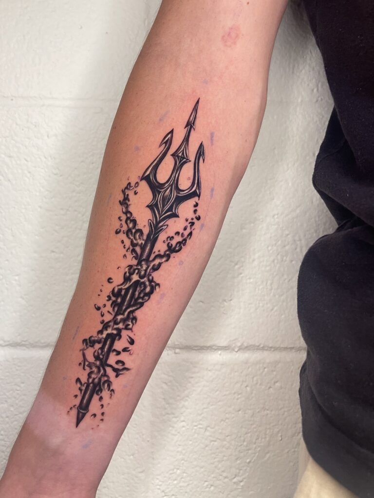 A black tattoo of a trident surrounded by swirling, bubbly ink on a forearm.