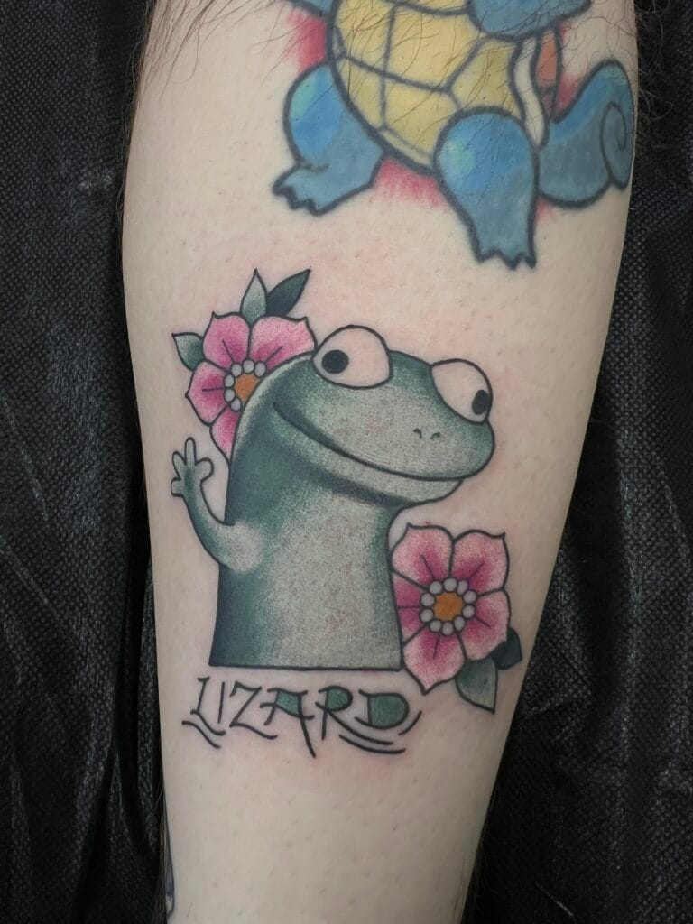 Cartoon lizard with pink flowers and Lizard text on arm tattoo.