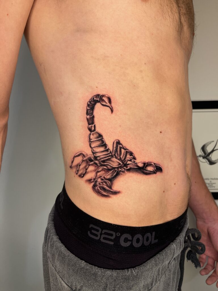 Black and gray scorpion tattoo on persons side torso, near the waist.