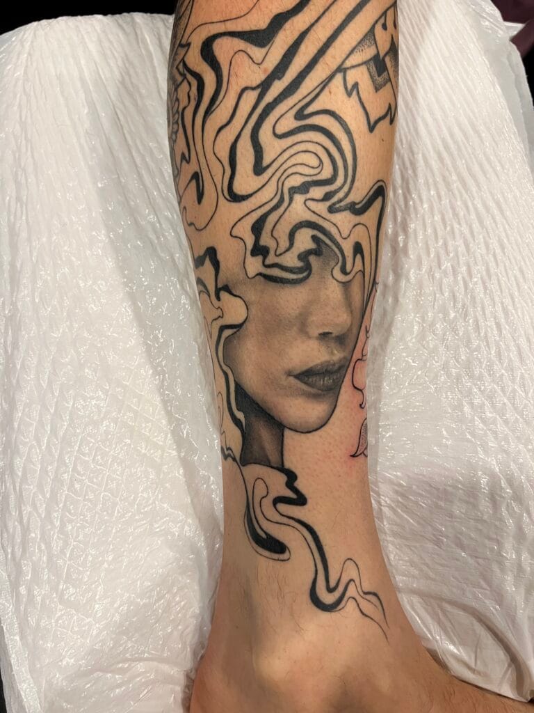 Black and gray tattoo of a womans face with flowing, abstract lines on the calf.