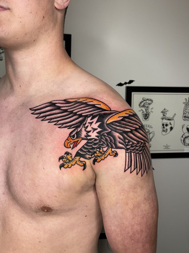 Bold black and orange eagle tattoo on persons shoulder and upper arm.